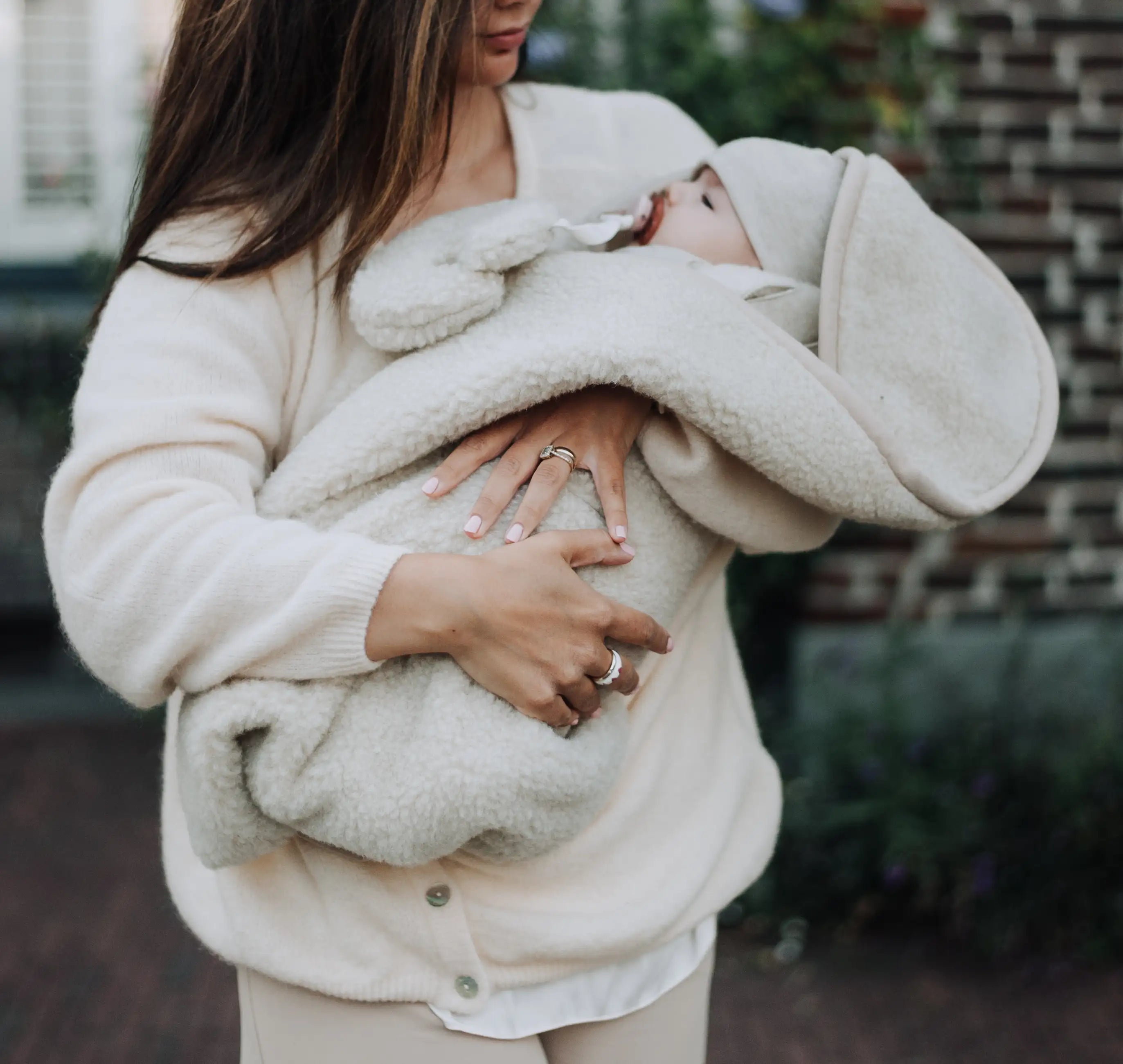 baby die in armen moeder ligt met merinowol knuffelmaantje