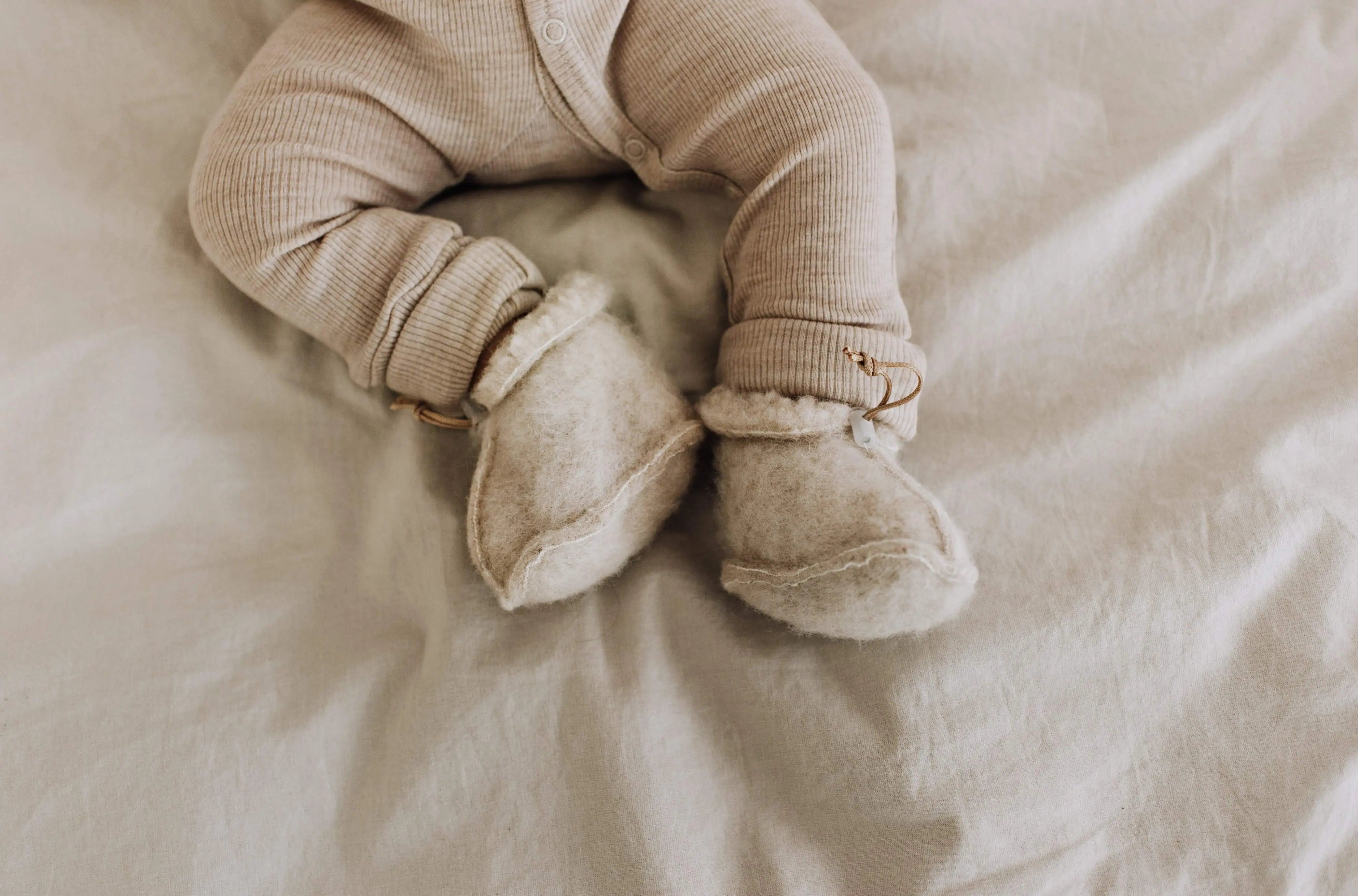 Liggende baby met Merinowol slofjes en een wollen boxpakje aan in de kleur naturel