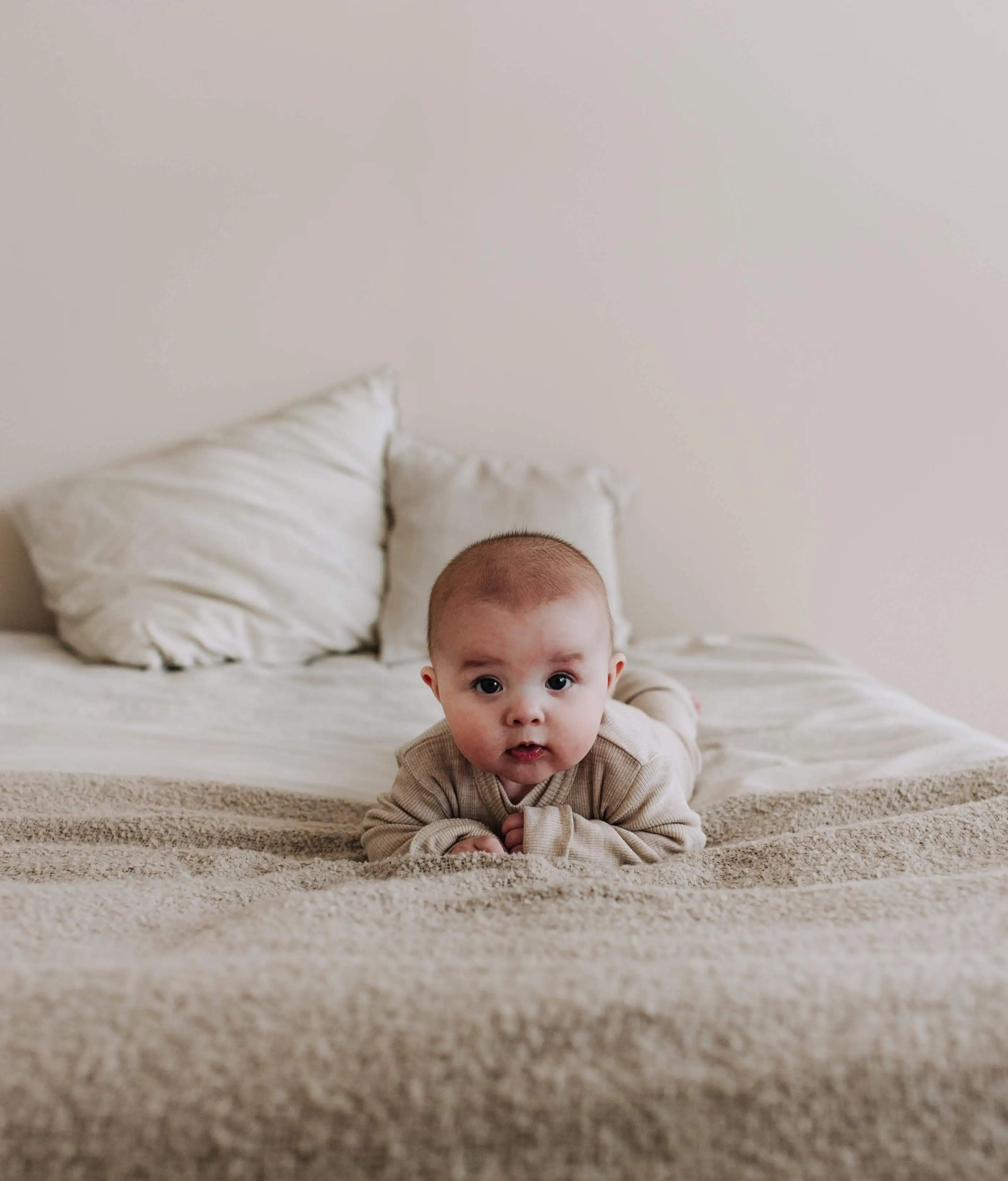 Baby met wollen boxpakje die op zijn buik ligt en in de camera kijkt
