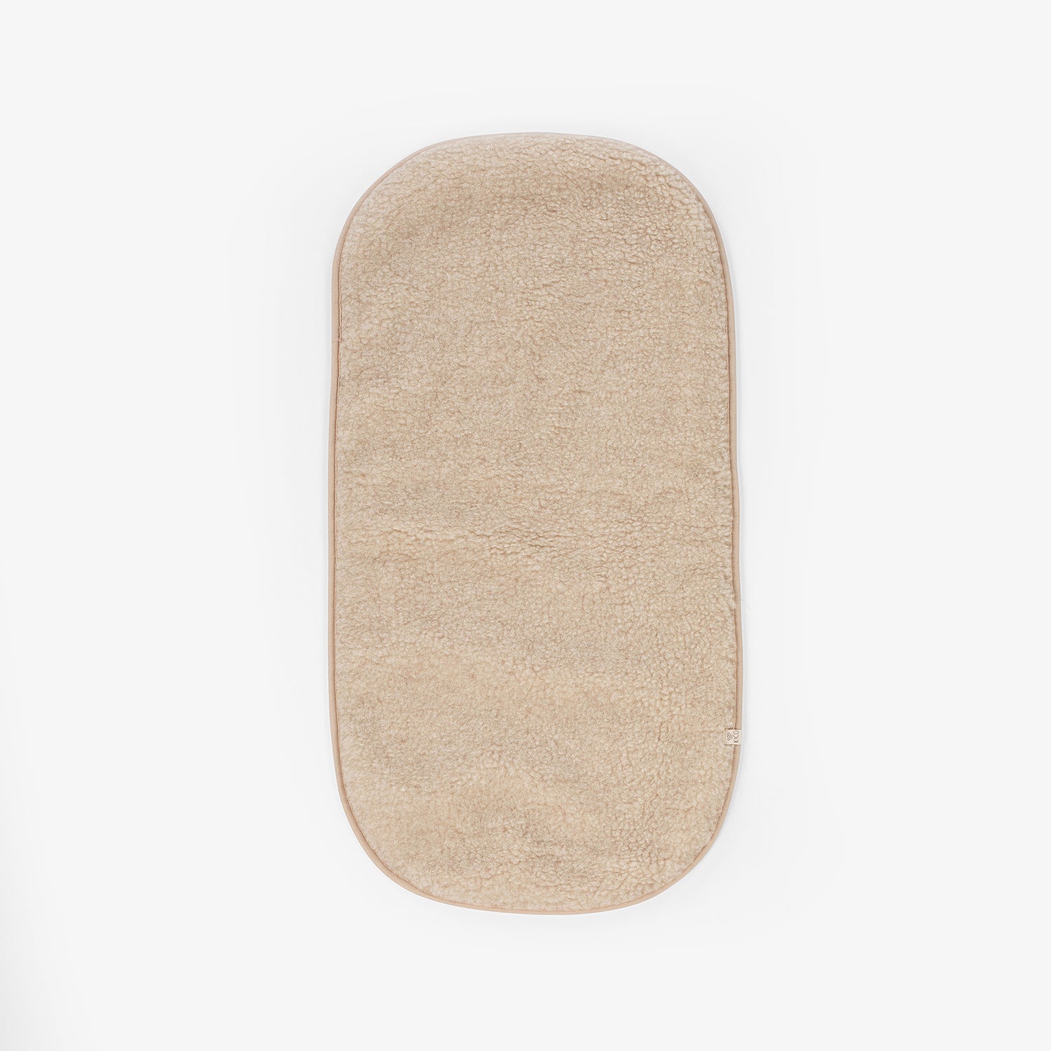 Productfoto van een wollen onderlegger in de kleur beige die gebruikt wordt in de wieg of ledikant tegen een witte achtergrond