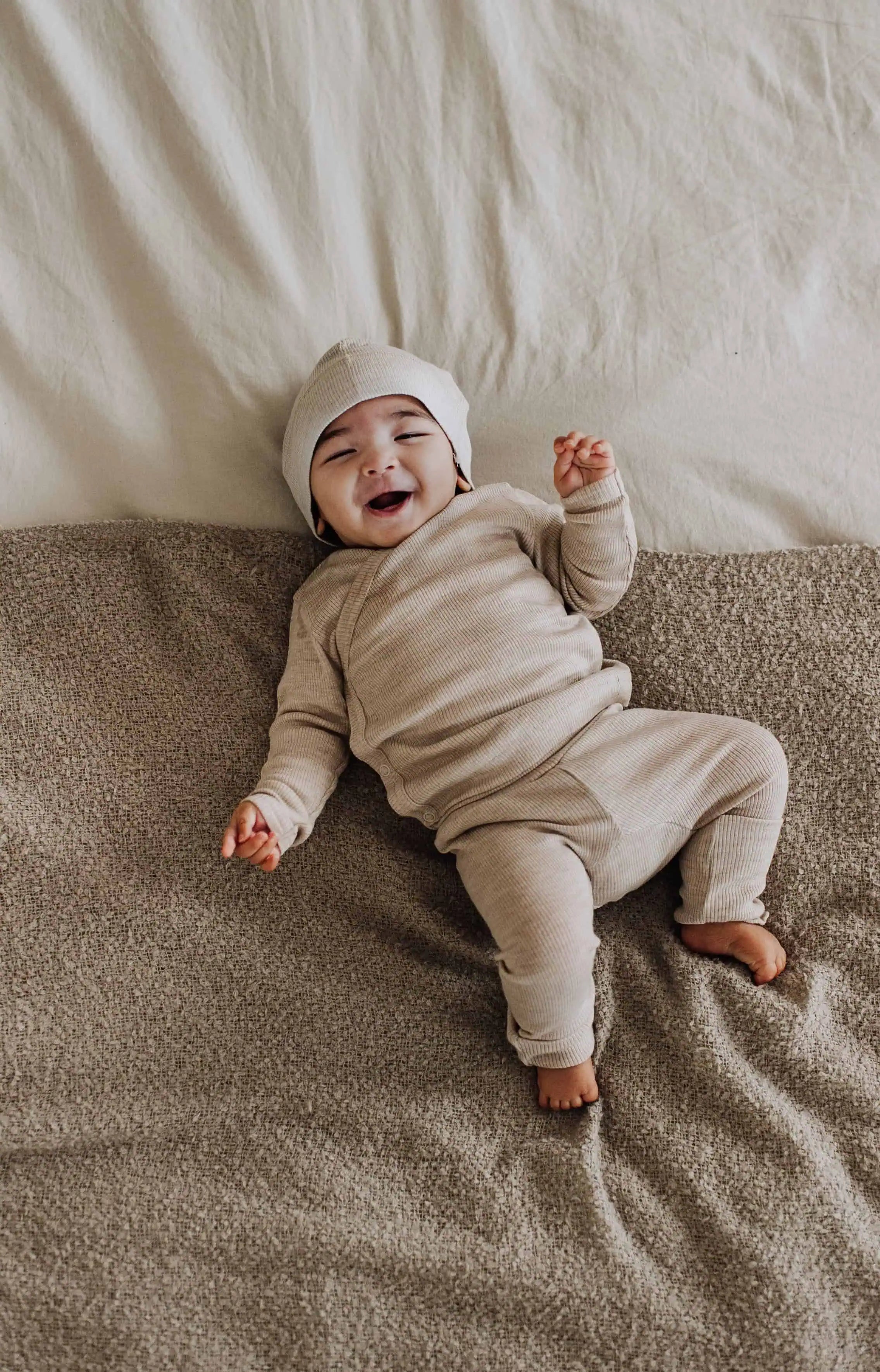Lachende baby in wollen overslag shirt en wollen broek liggend op bed