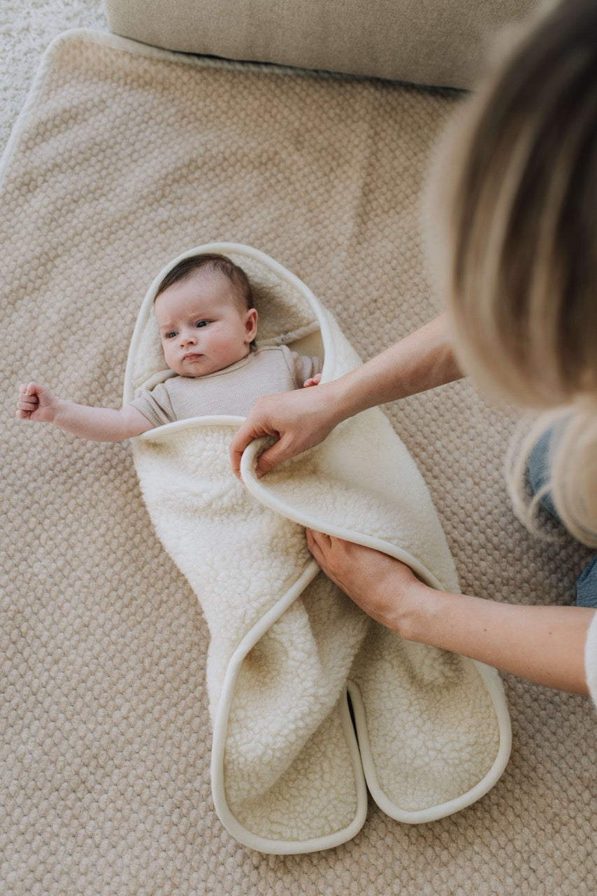 Baby wordt geborgen in wikkeldeken met capuchon en voetjes gelegd door mama
